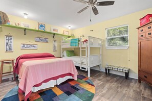 Ein Zimmer mit Etagenbett, Schreibtisch, Stuhl, einem Regal mit Bildern und einem Fenster mit Jalousien.