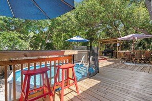 A wooden deck with a pool, outdoor seating, and a covered barbecue area. - Wooded area home with private pool, pool table, and outdoor amenities (Dauphin Island)