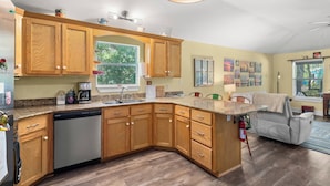 A kitchen with wooden cabinets, a dishwasher, a window, and a fire extinguisher. - Wooded area home with private pool, pool table, and outdoor amenities (Dauphin Island)