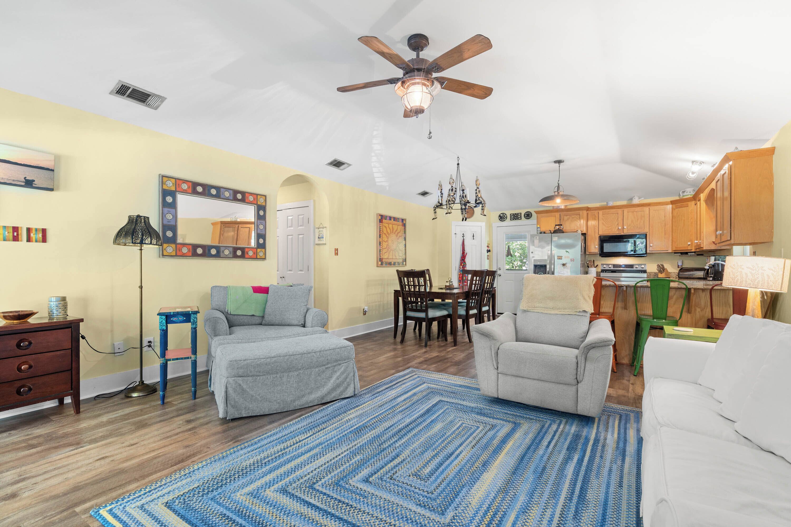 A living room with a ceiling fan, a dining area with a chandelier, and a kitchen with wooden cabinets.