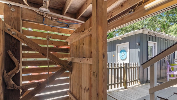 A wooden staircase leading to a deck area with a small building in the background. - Wooded area home with private pool, pool table, and outdoor amenities (Dauphin Island)