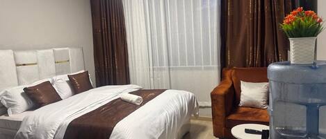 A hotel room with a bed, a sofa, a small table, a water dispenser, and a TV.