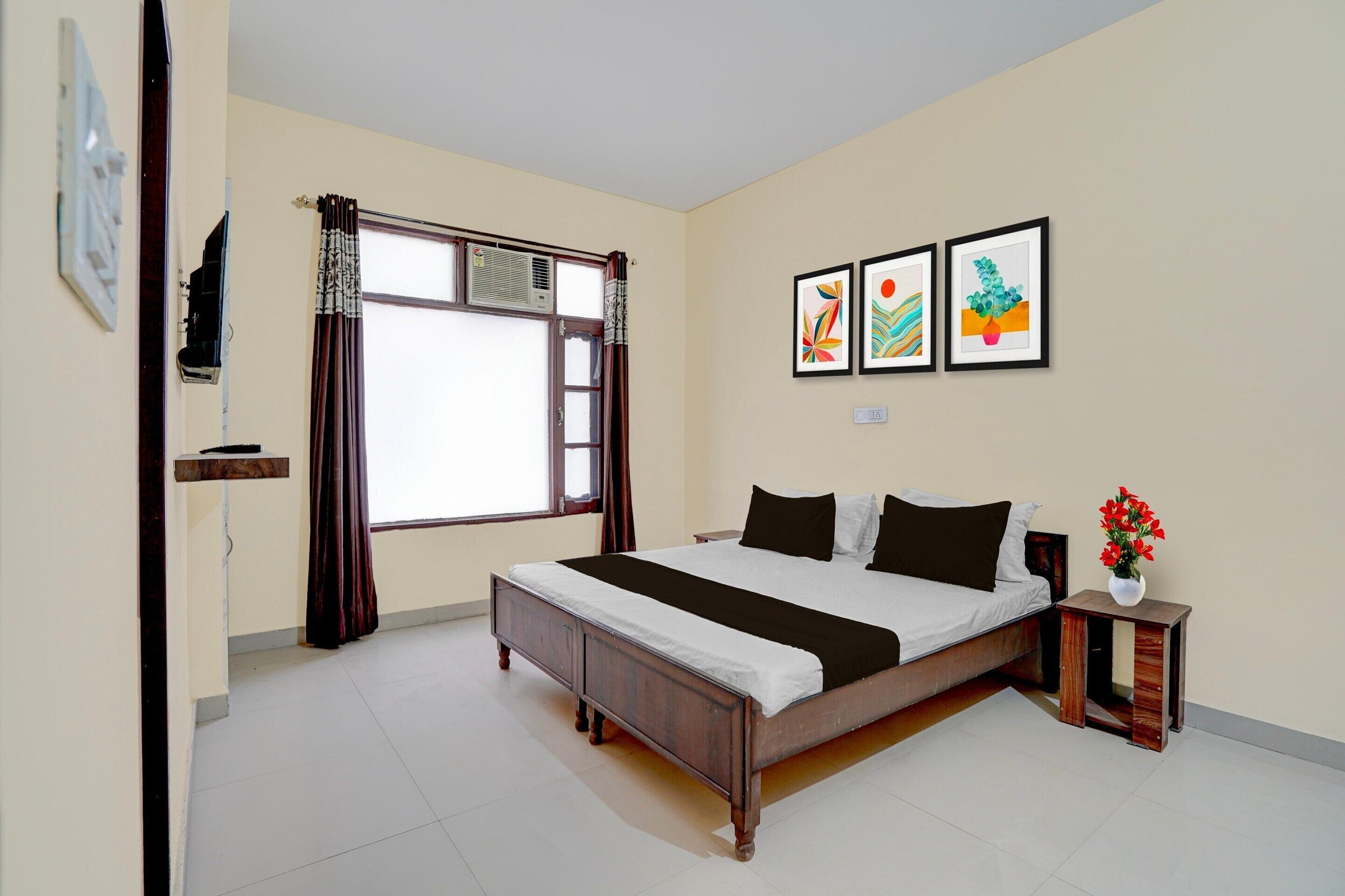 A bedroom with a bed, a nightstand, a window with curtains, and three framed pictures on the wall.
