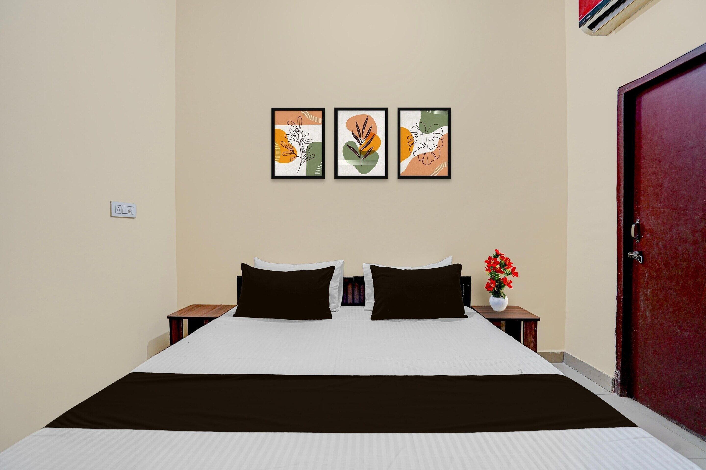 A hotel room with a bed, two nightstands, a red door, and three framed artworks on the wall.