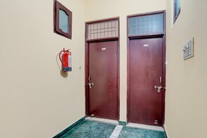 A hallway with two wooden doors, a fire extinguisher, and a small window. - Classic Ganesha (Kharar)