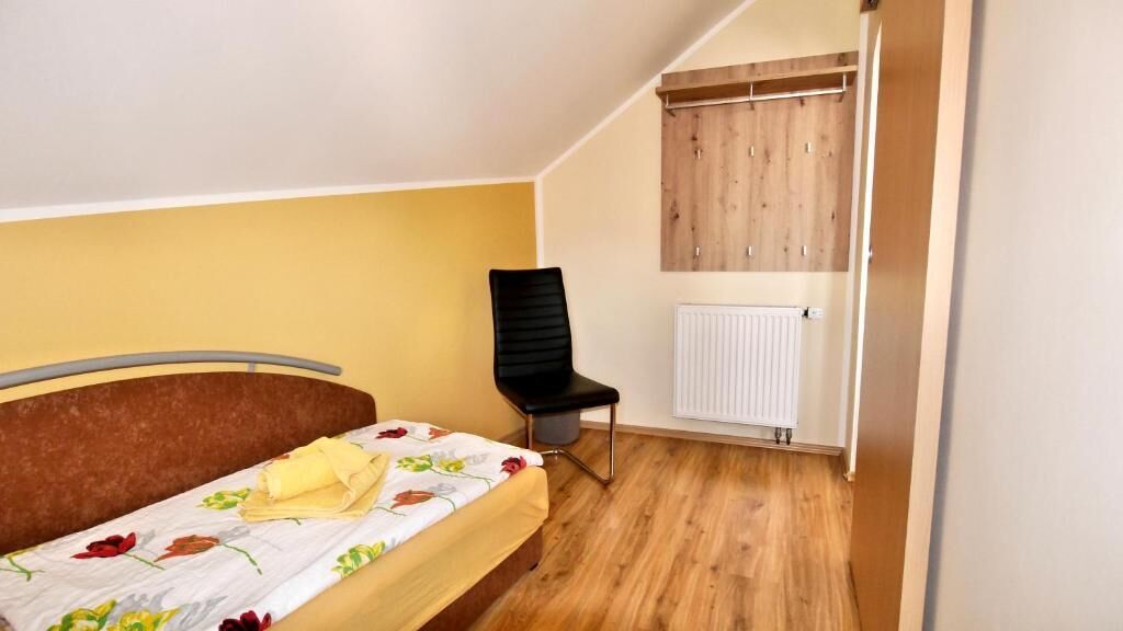 A bedroom with a bed, a chair, a radiator, and wooden wardrobe.
