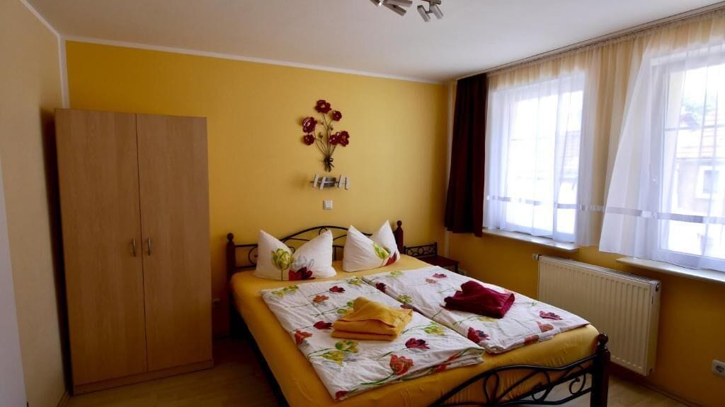 Ein Schlafzimmer mit Bett, Kleiderschrank, Heizkörper und einem Fenster mit Vorhängen.
