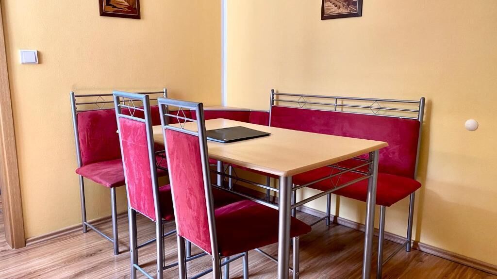 Un comedor con una mesa y cuatro sillas rojas acolchadas, una tableta negra sobre la mesa y una pared amarilla.