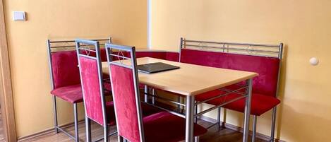 A dining area with a table and four red cushioned chairs, a black tablet on the table, and a yellow wall.