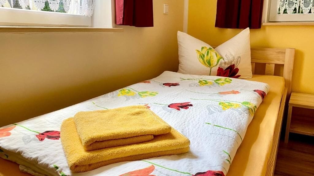 A single bed with a floral bedspread, a yellow towel, and a pillow with a floral design.