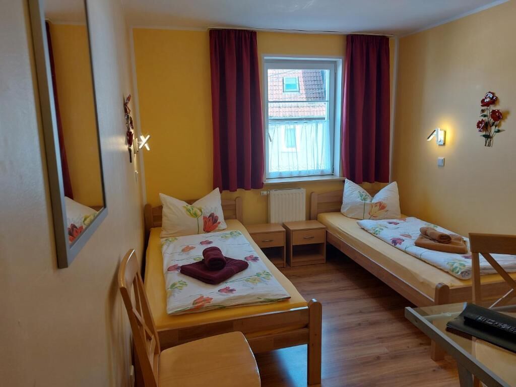 Een kamer met twee eenpersoonsbedden, een bureau, een stoel, een radiator en een raam met gordijnen.