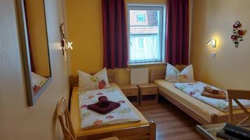 Ein Zimmer mit zwei Einzelbetten, einem Schreibtisch, einem Stuhl, einem Heizkörper und einem fenster mit Vorhängen.