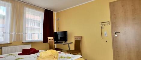 A hotel room with a bed, a desk with a TV, a chair, a door, and a window with curtains.
