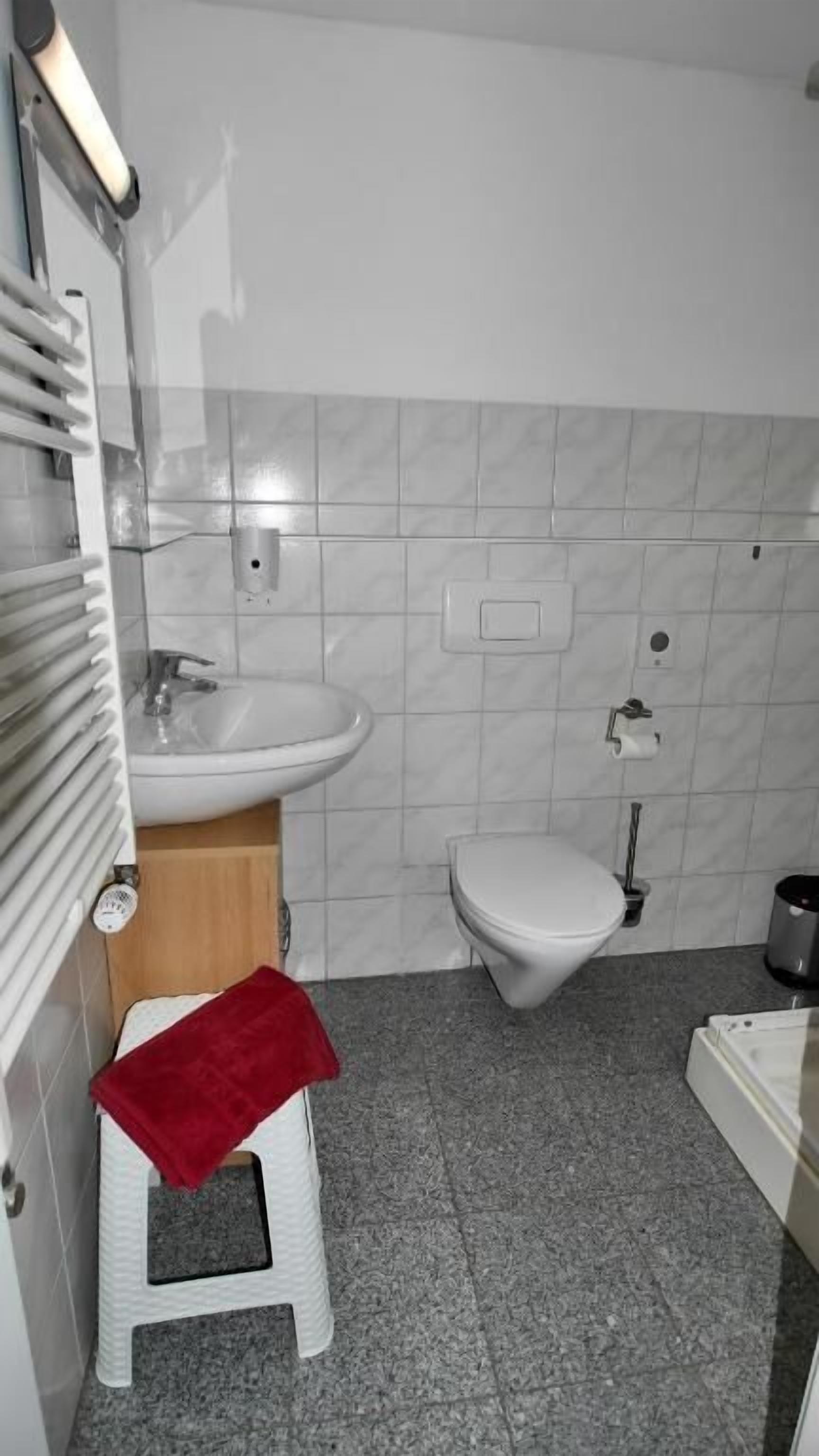 Un baño con lavamanos blanco, inodoro y un taburete pequeño con toalla roja.