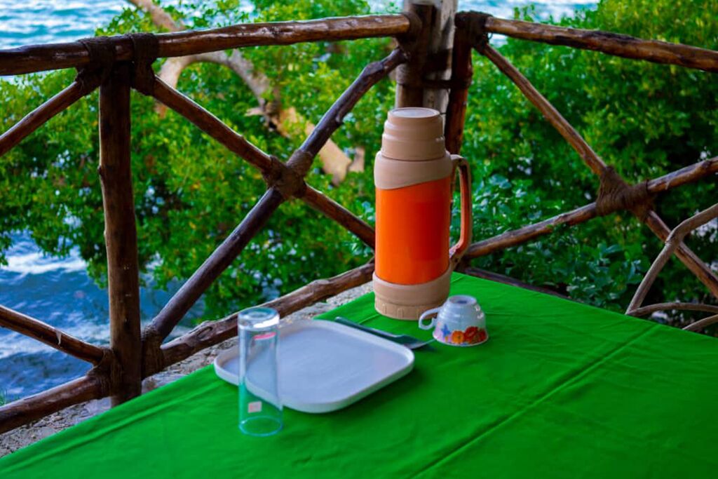 A table with a green tablecloth, a thermos, a glass, a teapot, and a plate.