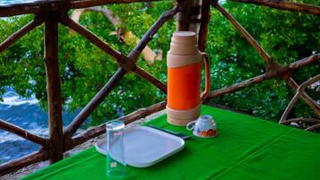 A table with a green tablecloth, a thermos, a glass, a teapot, and a plate.