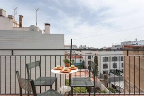 Un balcón con mesa y sillas, vista del paisaje urbano y un edificio blanco al fondo.