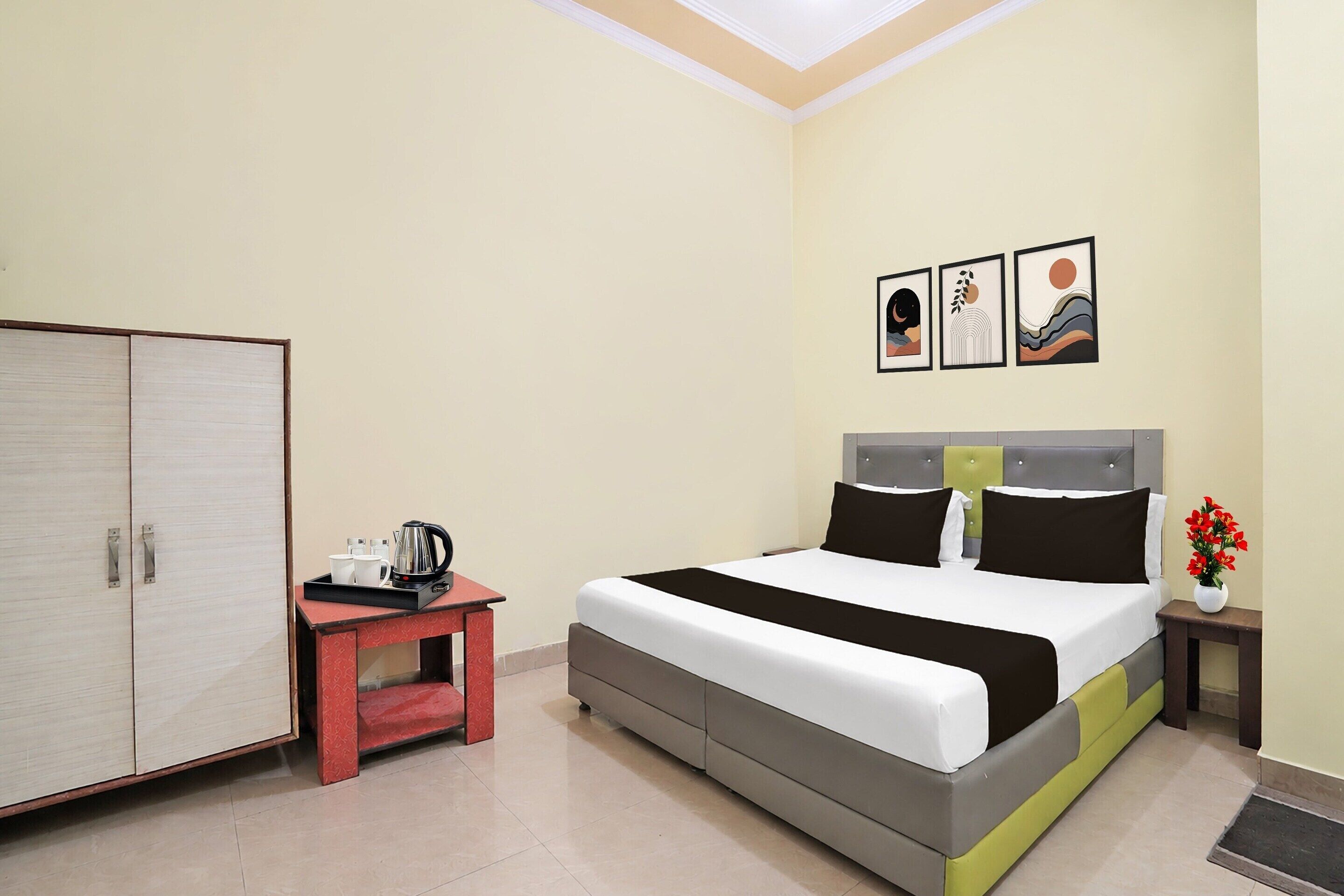 A hotel room with a bed, a wardrobe, a small table with a kettle, and a nightstand with a vase of flowers.