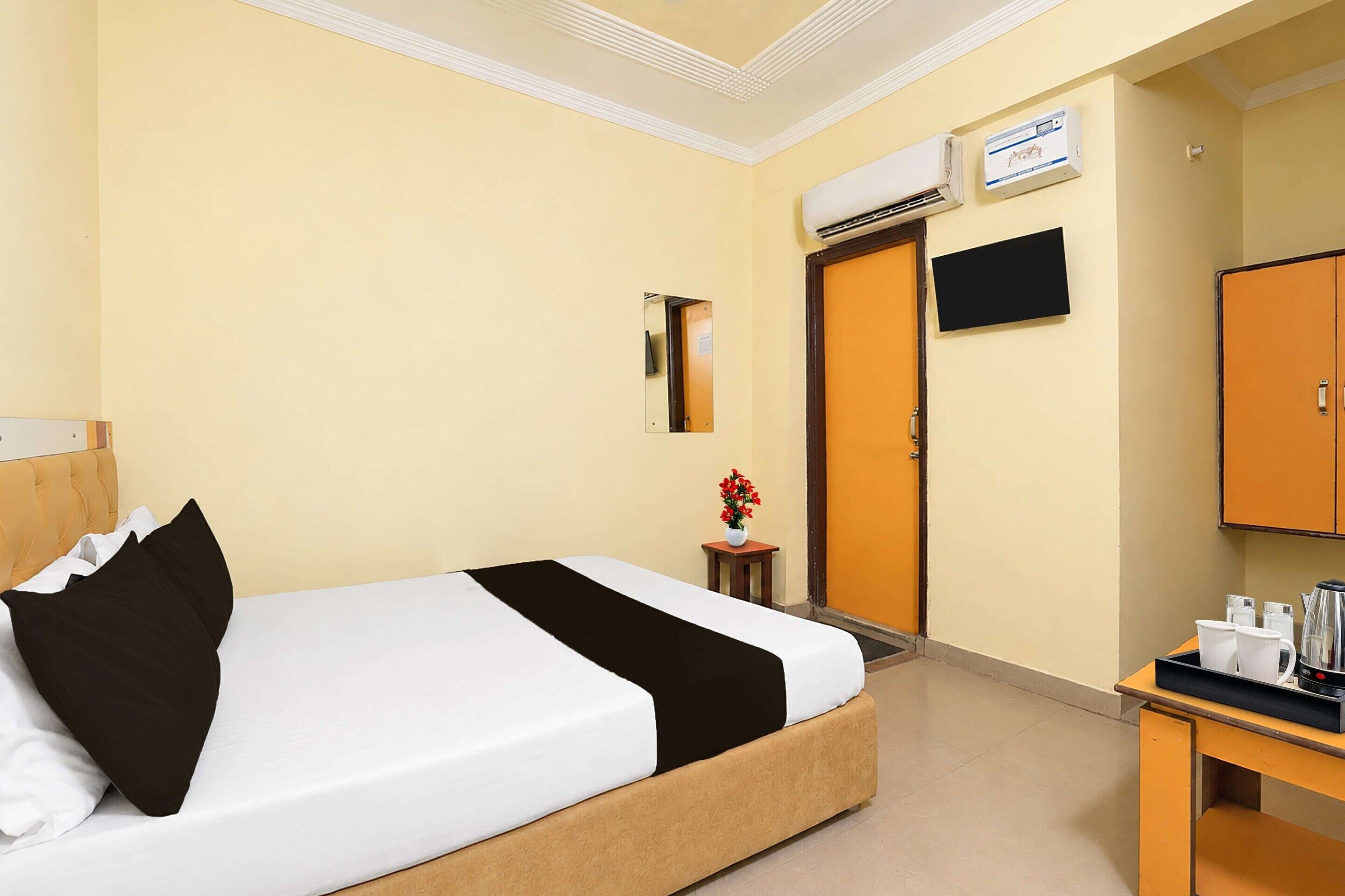 A hotel room with a bed, a desk with a coffee maker, a TV, and an air conditioning unit.
