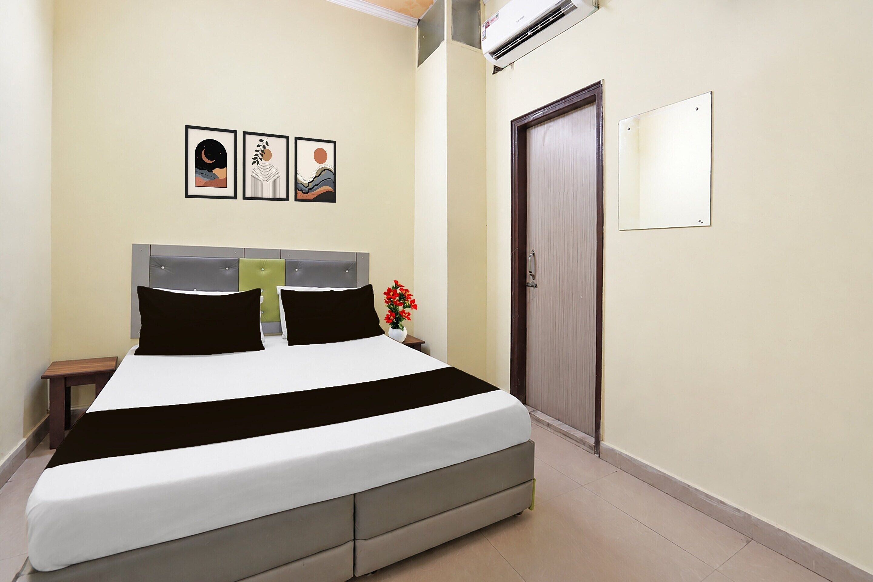 A hotel room with a bed, a nightstand, a wall-mounted air conditioner, and three framed pictures.