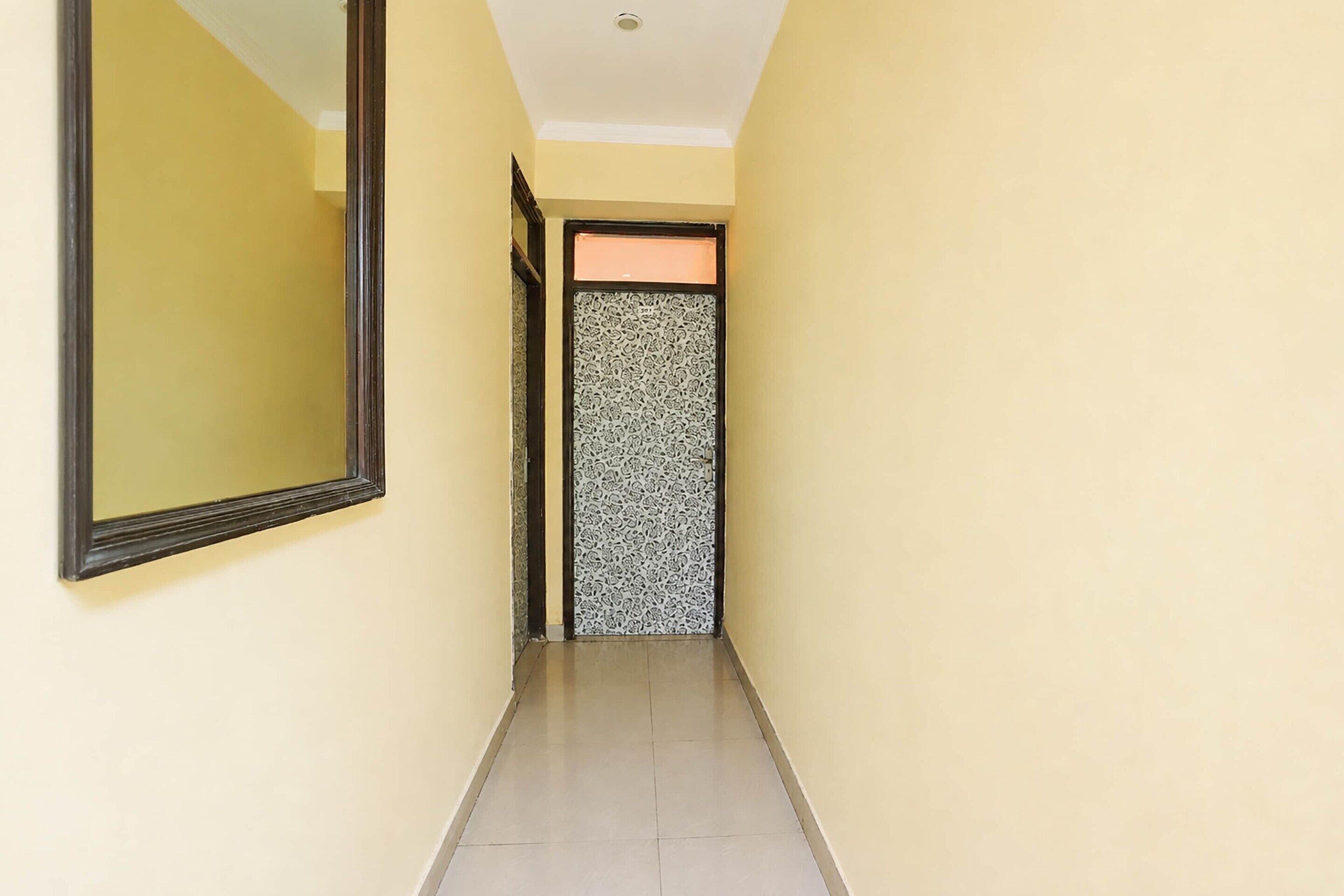 A narrow hallway with a mirror on the left and a patterned door at the end.