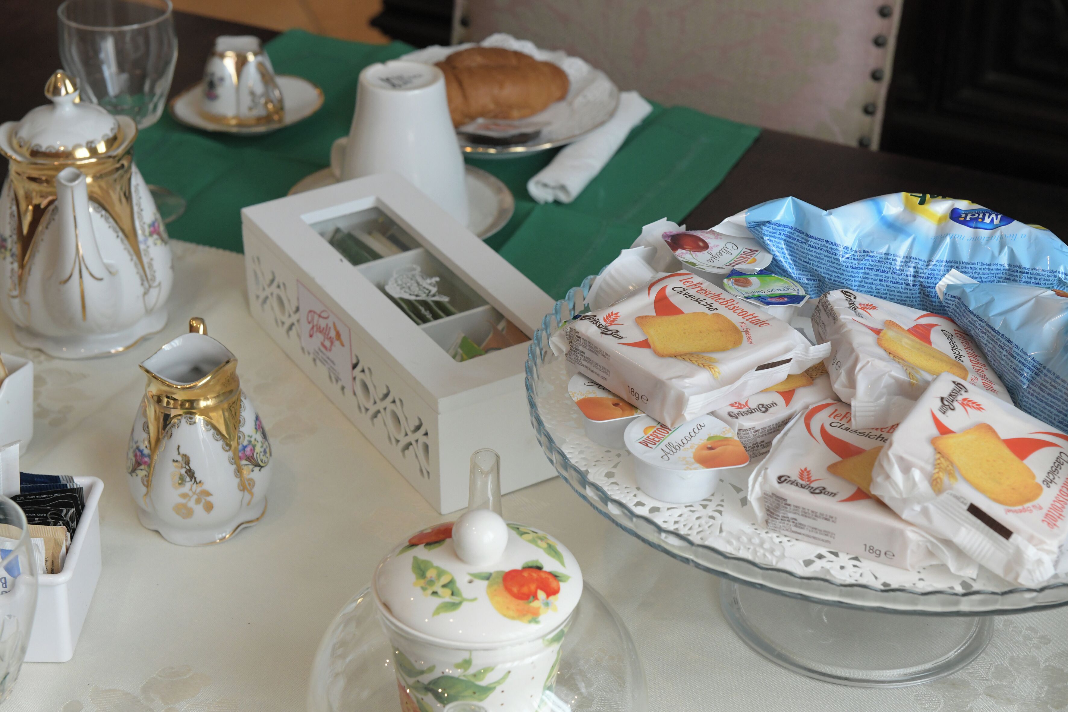 A table with a teapot, a pitcher, a box, and a plate with pastries.