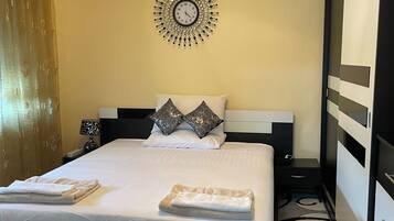 Quarto de hotel com cama, relógio de parede, mesa de cabeceira e criado-mudo.