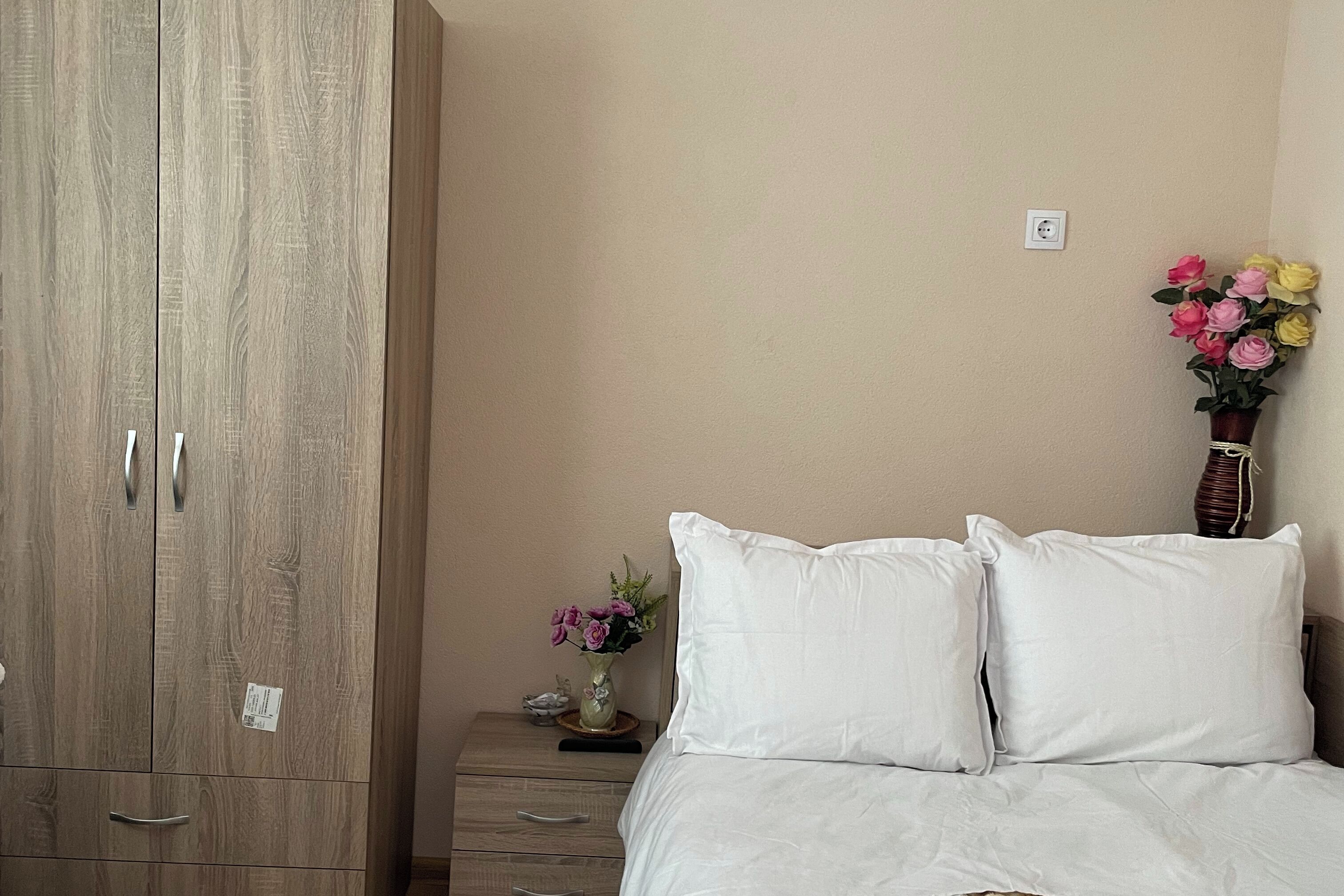 Una camera da letto con un'armadio in legno, un comodino con un vaso di fiori e un letto con biancheria bianca.