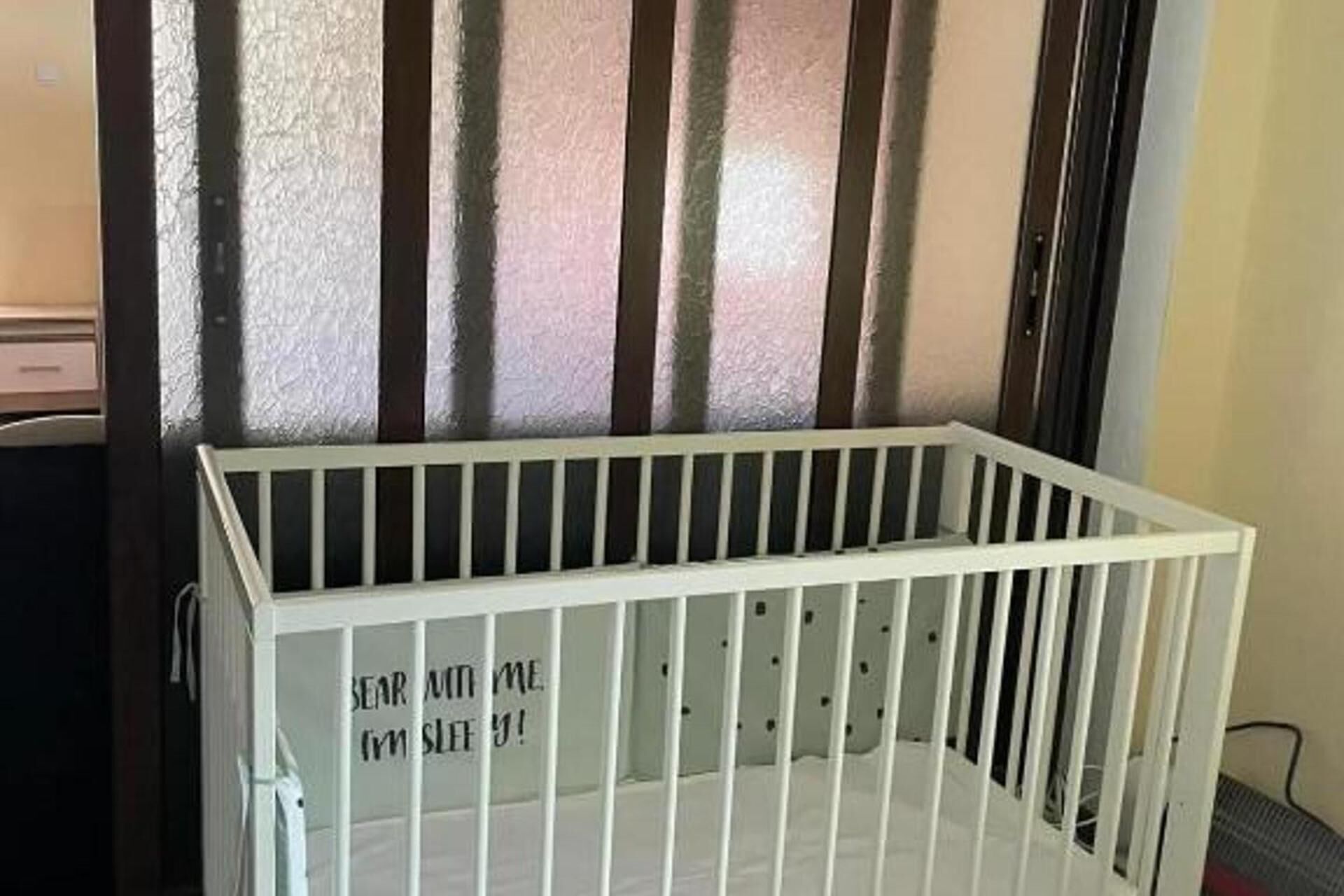Un berceau blanc à barreaux, placé contre un mur texturé orné de lignes verticales.