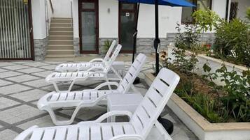 Cadeiras de descanso ao ar livre dispostas em fileiras, entrada de um edifício e um vaso com plantas.