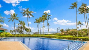A swimming pool with clear blue water, surrounded by palm trees and a view of the ocean. - Garden Condo Near Poipu Beach | Pool, Hot Tub & Tennis | Manualoha 203 (Koloa)