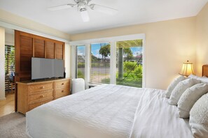 A modern bedroom with a large bed, a TV on a wooden dresser, and a ceiling fan. - Garden Condo Near Poipu Beach | Pool, Hot Tub & Tennis | Manualoha 203 (Koloa)