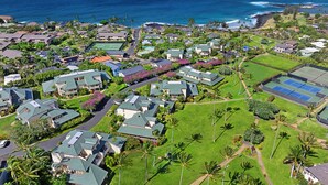 A residential area with houses, a tennis court, and a view of the ocean. - Garden Condo Near Poipu Beach | Pool, Hot Tub & Tennis | Manualoha 203 (Koloa)