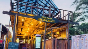 Een restaurant aan het strand met een houten constructie, een bord en een menukaart.