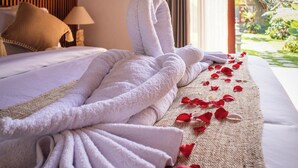 A neatly made bed with a white blanket and a rolled-up towel, a beige throw pillow, and a bedside lamp.