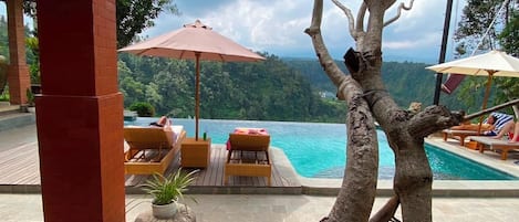 A poolside area with lounge chairs and umbrellas, overlooking a lush landscape.