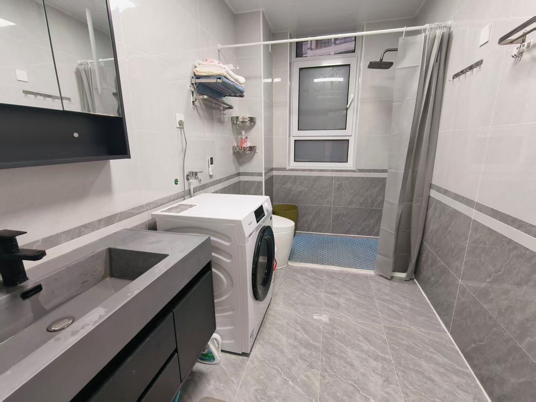 A modern bathroom with a washing machine, a sink, and a shower area.