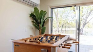 Ein Tischkicker in einem Raum mit großem Fenster, einer Topfpflanze und einer Klimaanlage an der Wand.