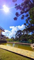 Zona de piscina con borde de piedra, rodeada de árboles y un edificio.