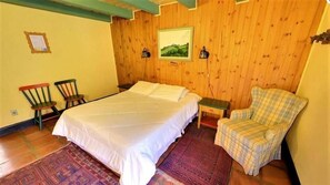 Una habitación con una cama, una silla, una mesita y un cuadro en la pared.