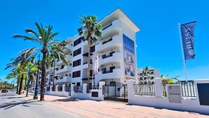 Un hotel de varios pisos con balcones, palmeras y un cielo azul despejado.