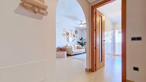 Un interior moderno con un pasillo que conduce a una sala de estar, que incluye un sofá blanco, arte decorativo en la pared y una puerta de madera.
