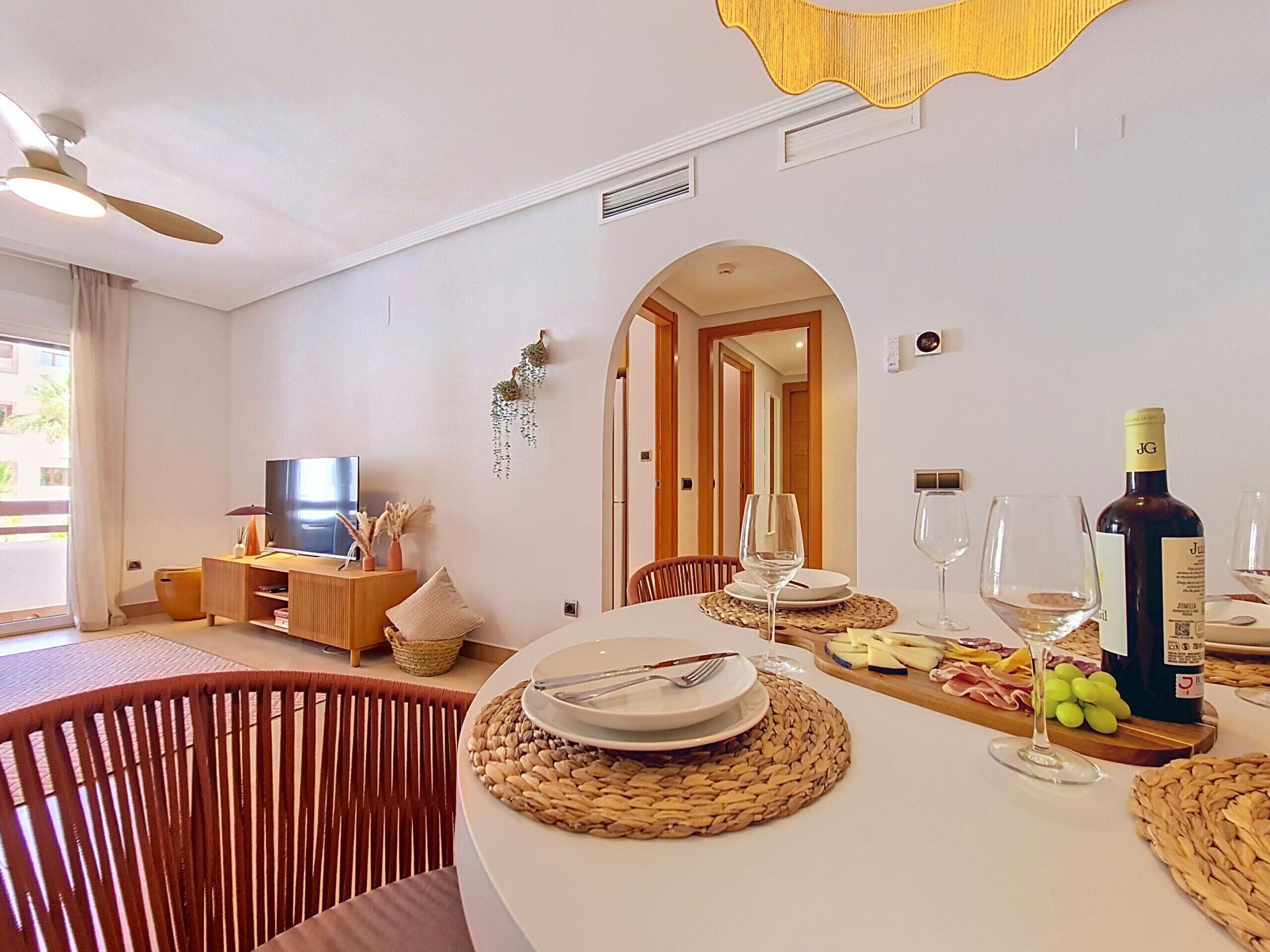 A dining area with a table set for two, a bottle of wine, and a television in the background.