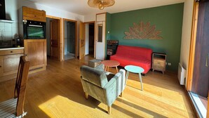 Ein kompakter Wohnbereich mit Küchenzeile, Essbereich und einer Sitzecke mit rotem Sofa und rundem Tisch.