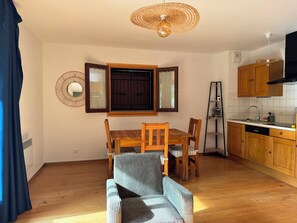 Ein Essbereich mit Holztisch und -stühlen, eine Küche mit Holzschränken und einer Deckenleuchte.
