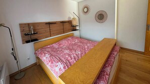 Ein Schlafzimmer mit einem Bett, einem Holz-Kopfteil, einem Nachttisch, einer Stehlampe und dekorativen Wandspiegeln.