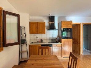 A modern kitchen with wooden cabinets, a built-in oven, and a dining area with a wooden table. - New—Cozy Apartment in a Terrace Chalet in Les Houches—Mont Blanc (Les Houches)
