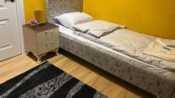 Un lit simple avec une tête de lit à motifs, une table de chevet avec un miroir et un tapis rayé noir et blanc.