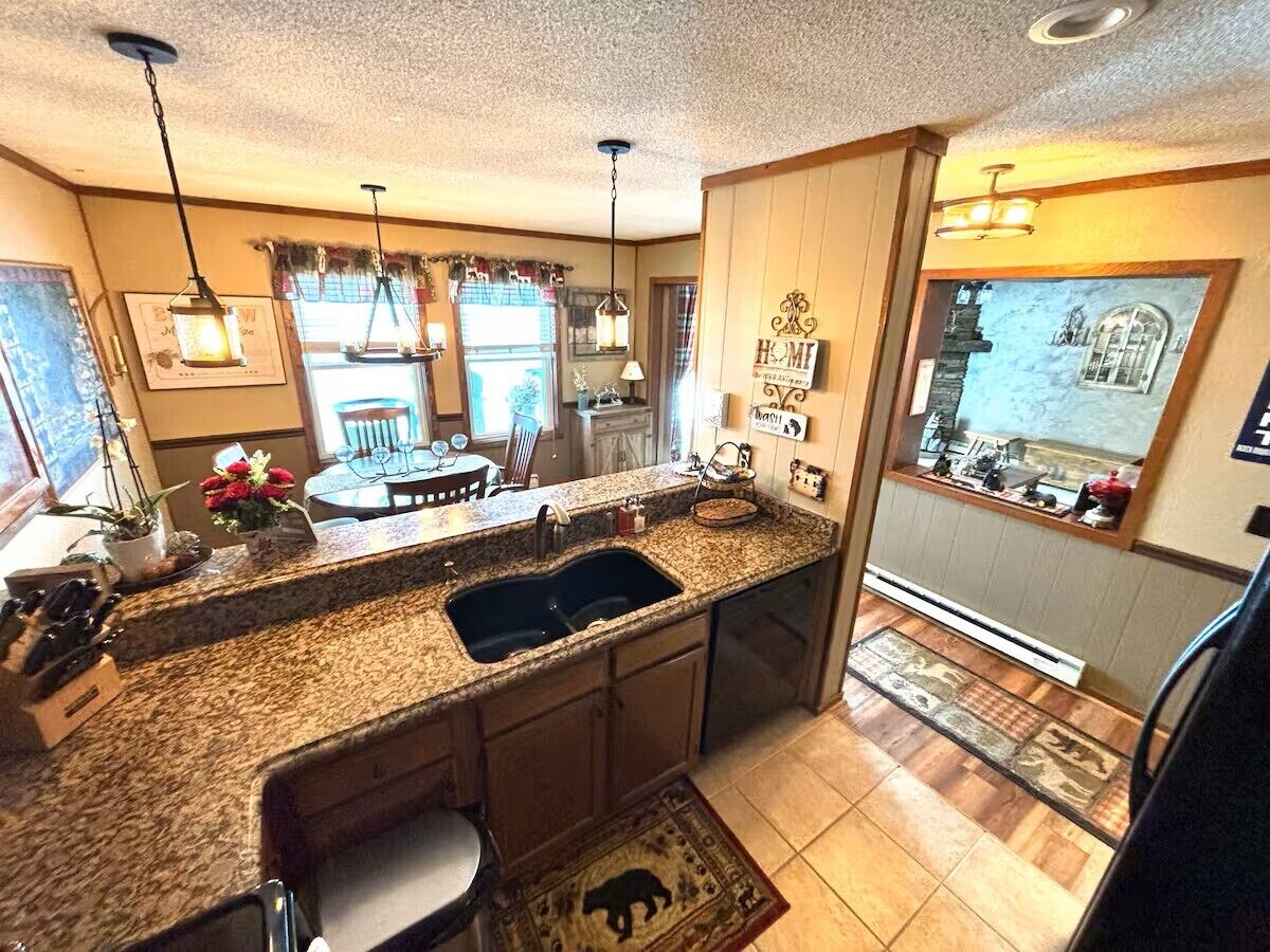 A kitchen with granite countertops, a double sink, pendant lighting, and a view of the backyard.