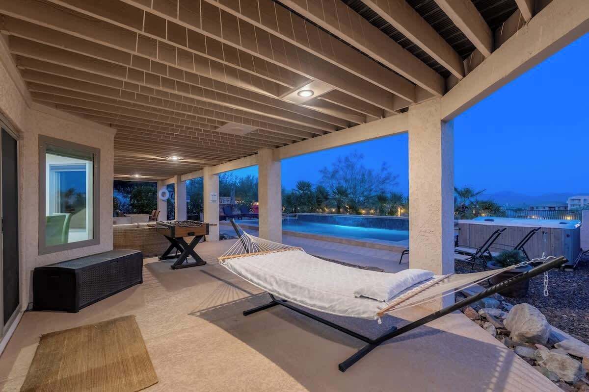 A covered outdoor area with a hammock, seating, and a view of a swimming pool at dusk.